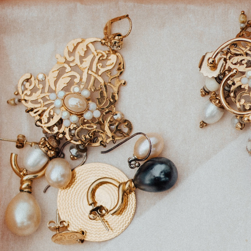 Gold colored earrings with white and black pearls laying down.