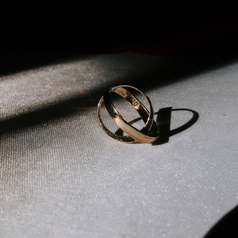 Two gold rings intertwined, photographed with shadows in the back.